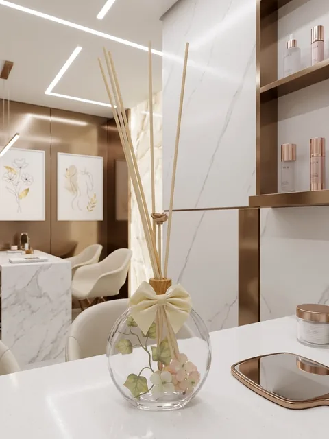 Difusor de ambiente em vidro redondo com folhas e flores rosadas dentro, laço creme e varetas naturais, em clínica de estética
