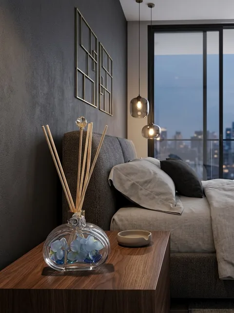 Difusor de ambiente em vidro transparente com flores azuis e pedras de vidro dentro, sobre criado-mudo em quarto com vista noturna da cidade