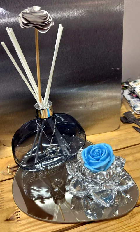 Kit com difusor de ambiente em vidro fumê com pingente prateado e vela em formato de rosa azul sobre lótus de cristal, apoiados em uma bandeja espelhada