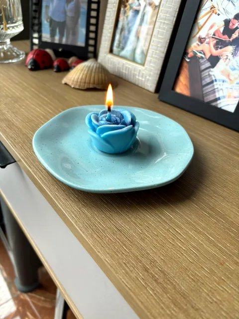 Vela em formato de rosa azul, acesa, sobre um pratinho de cerâmica turquesa