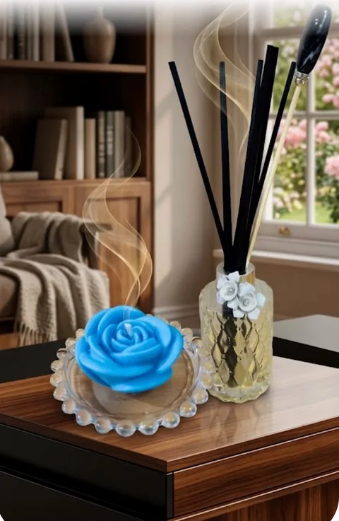 Vela em formato de rosa azul em prato de vidro com bolinhas, ao lado de difusor em vidro lapidado dourado com flores brancas e varetas pretas